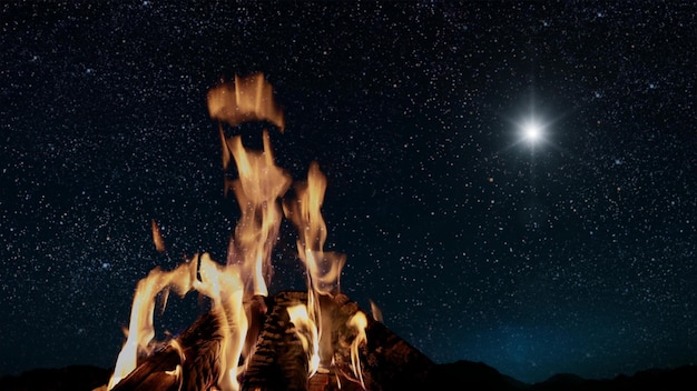 Foto la hoguera arde por la noche contra el fondo de las montañas y el mar con estrellas brillantes