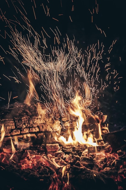 Hoguera ardiente con llamas naranjas brillantes y chispas y carbón caliente contra el cielo nocturno oscuro