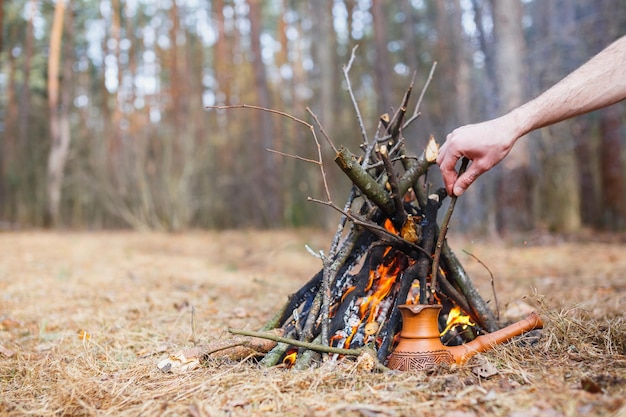 En la hoguera en el bosque de primavera, una cafetera turca de arcilla se calienta contra la hierba En el marco, la mano de un hombre