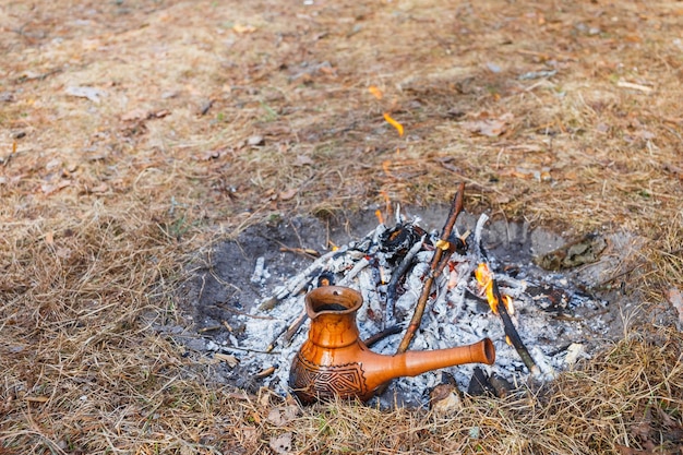 En la hoguera en el bosque de primavera, una cafetera turca de arcilla se calienta contra la hierba