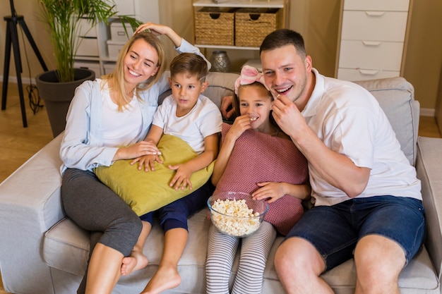 Hohe Ansichtfamilie, die Popcorn isst und auf Couch sitzt