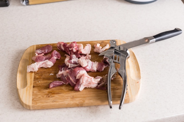 Hohe Betrachtungswinkel von rohen Fleischstücken, Messern und Küchengeräten auf Holzbrett auf weißer Arbeitsplatte - geschnittenes Fleisch, das zum Kochen zubereitet wird