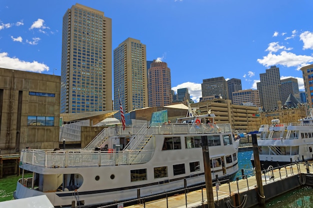 Hohe Gebäude und festgemachte Fähren mit Menschen in der Bucht von Boston, USA. Die Stadt ist von verschiedenen Wasseranlagen umgeben
