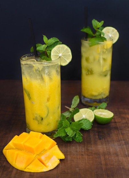 Hohe Gläser mit Mango-Mojito auf Holztisch und schwarzem Hintergrund