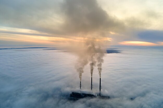 Hohe Rohre des Kohlekraftwerks mit schwarzem Rauch, der sich nach oben bewegt und die Atmosphäre verschmutzt Erzeugung elektrischer Energie mit fossilem Brennstoffkonzept