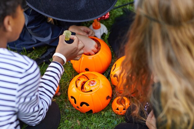 Hohe Winkelansicht bei Gruppe von Kindern, die Kostüme tragen, die Süßigkeiten von Halloween-Eimern im Freien nehmen, Raum kopieren