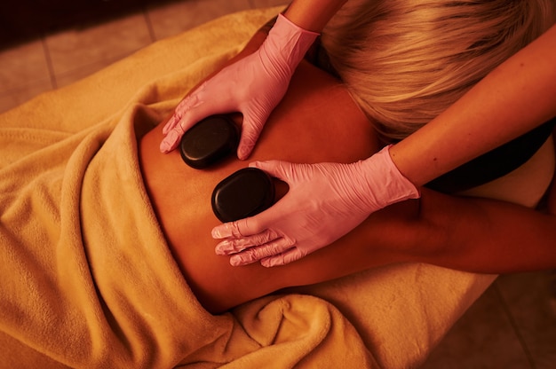 Hohe Winkelansicht der jungen Frau, die im Spa-Salon während der Hot-Stone-Massagesitzung entspannt