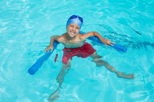 Hohe Winkelansicht des fröhlichen Jungen, der mit Poolnudel schwimmt