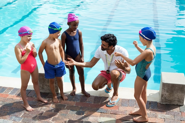 Hohe Winkelansicht des männlichen Trainers, der Kinder am Pool unterstützt