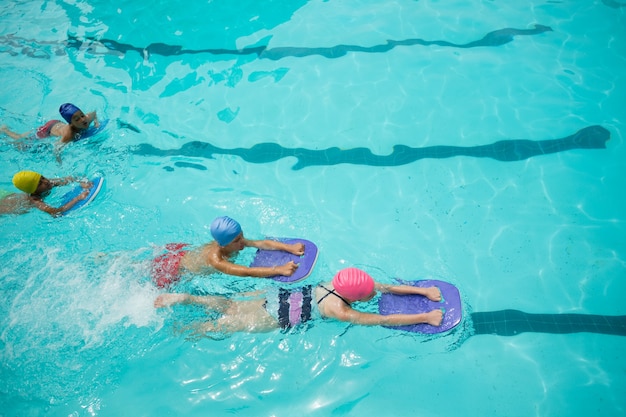 Hohe Winkelansicht von Mädchen und Jungen, die Kickboard beim Schwimmen im Pool verwenden