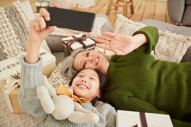 Hohe Winkelansicht von Mutter und Tochter, die winken und lächeln, während sie online unter Verwendung des Mobiltelefons sprechen
