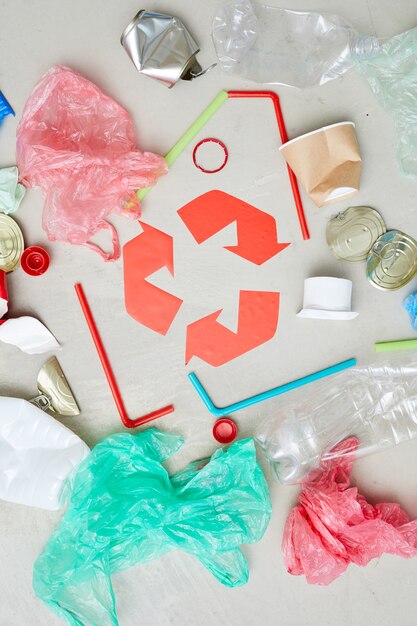 Hohe Winkelansicht von Verpackungsflaschen und -dosen um das rote Recycling-Symbol