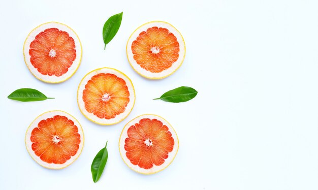 Hoher Vitamin C. Saftige Grapefruitscheiben mit grünen Blättern auf weißem Hintergrund.