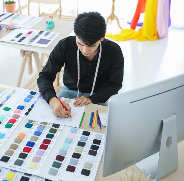 Hoher Winkel des asiatischen Modedesigners, der beim Sitzen am Tischprofi eine bunte Skizze erstellt