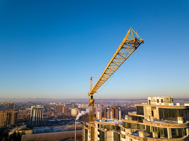 Hohes Gebäude der Wohnung oder des Büros im Bau, Draufsicht. Turmkran auf hellem Kopienraumhintergrund des blauen Himmels, Stadtlandschaft, die zum Horizont ausdehnt. Luftaufnahmen mit Drohnen.