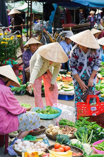 Hoi An, Vietnã - 17 de fevereiro de 2016: Comerciantes asiáticos vendendo legumes frescos para clientes no mercado de rua em Hoi An, Vietnã.