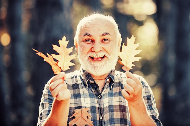 Hoja de arce en la ruta de senderismo en el parque Hombre senior feliz mirando a la cámara Retrato de otoño del abuelo