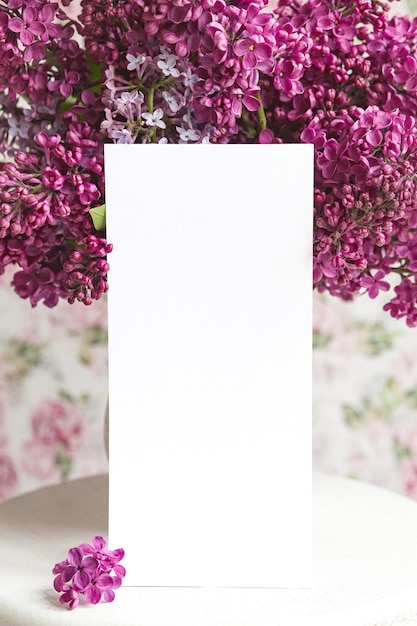 Hoja blanca en florecientes flores lilas violetas violetas sobre un soporte blanco sobre un fondo floral. Tarjeta de felicitación, lugar para texto, maqueta