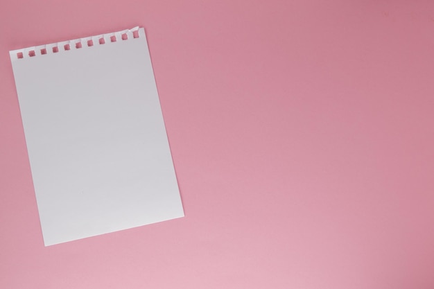 Una hoja blanca de papel arrancada de un cuaderno sobre un fondo rosa con una copia del espacio