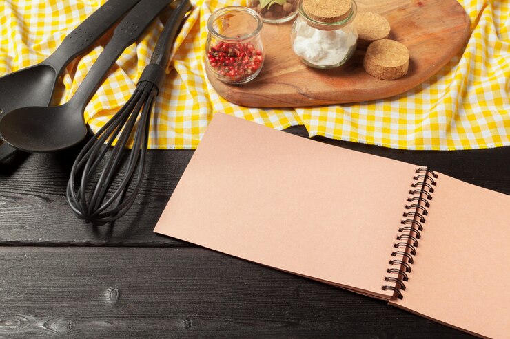 Foto hoja en blanco de bloc de notas abierto y utensilios de cocina en la mesa con mantel, espacio de copia