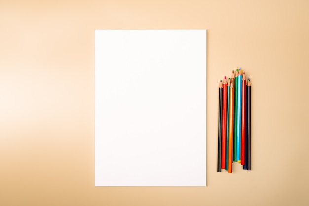 Una hoja en blanco y lápices de colores para dibujar sobre un fondo de textura simple con espacio para copiar y rotular. Diseño, maqueta de espacio libre.