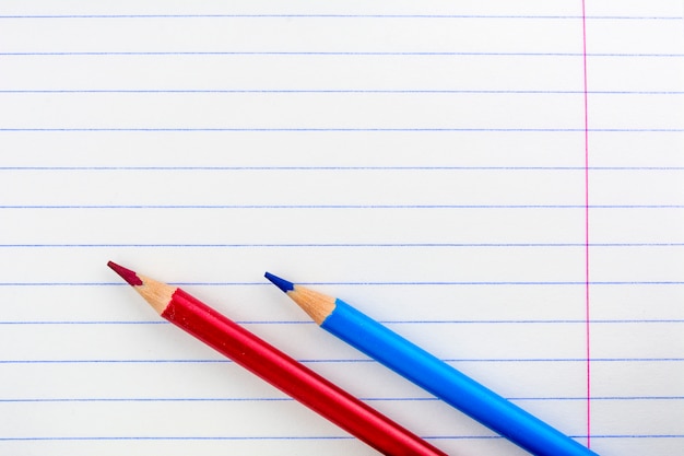 Hoja de un cuaderno escolar en la gama. Dos lápices en la hoja. Lápices rojos y azules.