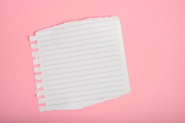 Hoja de cuaderno forrada con bordes rasgados sobre un fondo rosado