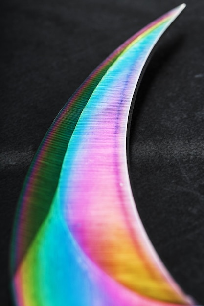 La hoja curva y afilada de la Kerambit Dagger es un color arco iris degradado sobre un fondo oscuro. Acero frío, primer plano