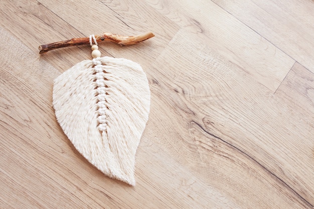 Hoja de macramé en color natural y devanados de hilo sobre una mesa de madera. Macramé de decoración de cuerda de algodón para hacer tu habitación más acogedora y única. Afición de la mujer. Decoración hecha a mano para colgar en la pared. Copia espacio