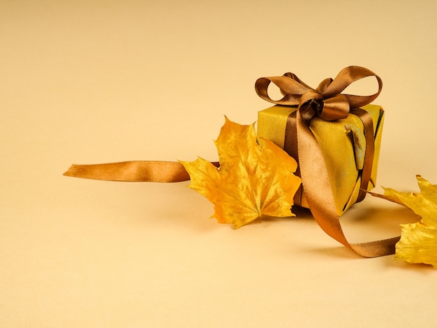 Una hoja de oro solitaria y una hoja pintada en el metal amarillo, el espacio para texto junto a una caja de regalo de vacaciones y cinta dorada