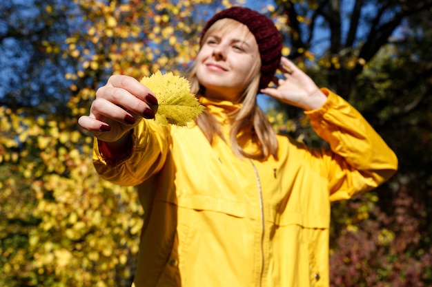 Una hoja de otoño amarilla en la mano de una mujer borrosa con el telón de fondo de las hojas de otoño. de cerca