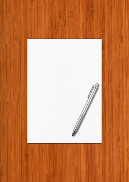 Hoja de papel A4 en blanco y bolígrafo sobre fondo de madera oscura.