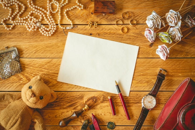 Una hoja de papel en blanco para escribir una carta en una mesa de madera con algunos recuerdos y joyas.