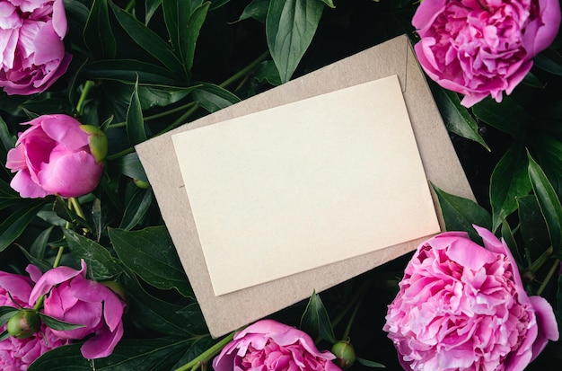 Hoja de papel en blanco y sobre artesanal sobre un fondo natural de flores de peonía rosa