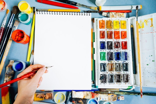 Hoja de papel blanco sobre un fondo de pinceles y pinturas multicolores