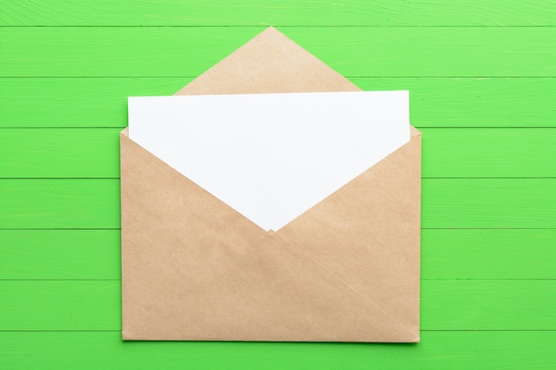 Una hoja de papel en blanco con un sobre sobre fondo de madera verde