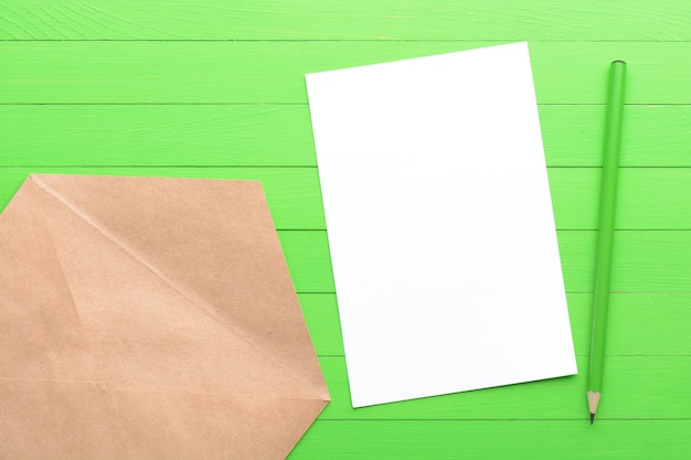 Una hoja de papel en blanco con un sobre sobre fondo de madera verde