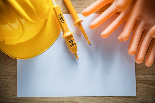 Hoja de papel guantes dieléctricos protectores casco de construcción probador eléctrico en tablero de madera.