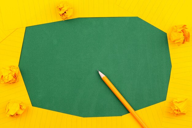 Foto una hoja de papel naranja se encuentra en una junta escolar verde que constituye un marco para el texto. cerca de lápiz y páginas arrugadas. copia espacio vista plana superior concepto educación.