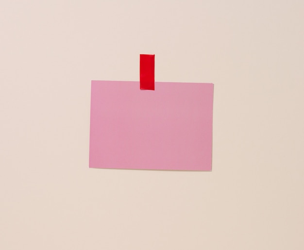 Hoja de papel rosa rectangular en blanco pegada sobre un fondo azul claro. Lugar para una inscripción, anuncio.