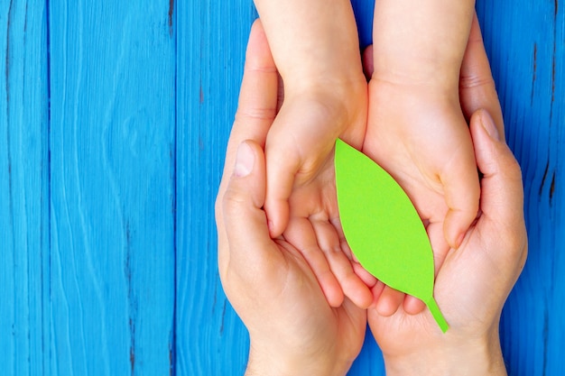 Hoja de papel verde en manos de adultos y niños.