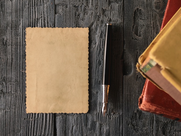 Una hoja de papel viejo y una pluma estilográfica con libros sobre madera.