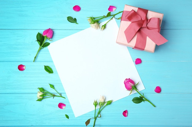 Hoja de rosas de papel y caja de regalo sobre fondo de madera