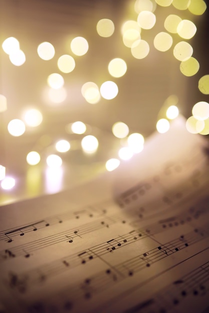 Foto hoja vieja con notas musicales de navidad como fondo contra luces borrosas. concepto de música navideña