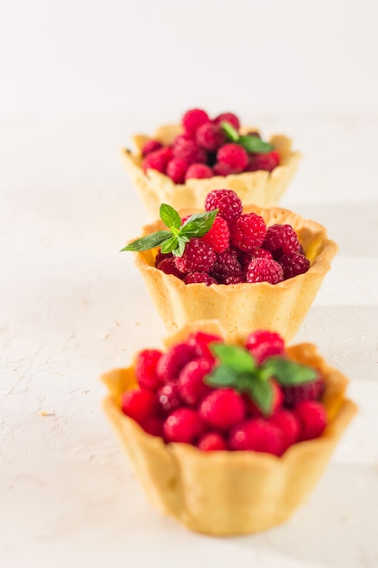 Foto hojaldre casero de frambuesa y pasta quebrada. mini tartaletas de bayas de verano con natillas de vainilla y hojas de menta. postres frescos en el fondo blanco aislado. espacio de copia gratuito.