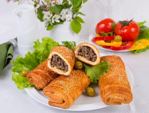 hojaldre relleno de hígado de carne, sobre un plato blanco con verduras sobre un fondo claro