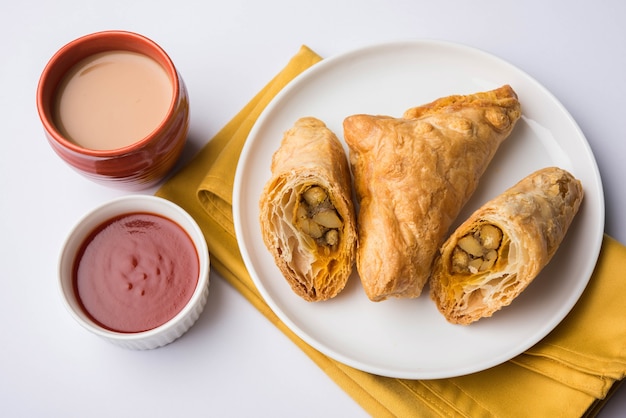 Hojaldre de verduras rellenas o samosa, famoso snack de panadería india, servido con salsa de tomate y té caliente, enfoque selectivo