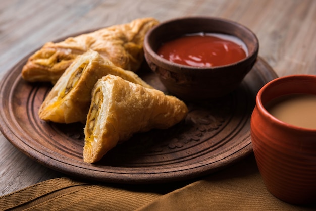 Hojaldre de verduras rellenas o samosa, famoso snack de panadería india, servido con salsa de tomate y té caliente, enfoque selectivo