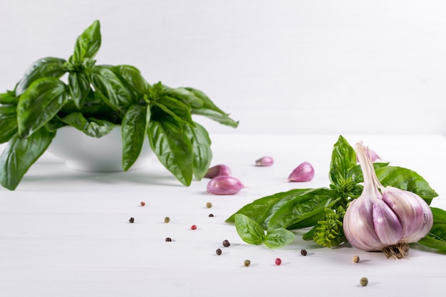 Hojas de albahaca verde fresca con ajo y pimienta sobre superficie blanca