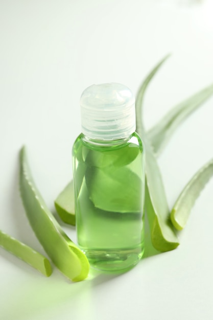 Hojas de aloe y botella con gel sobre fondo blanco.